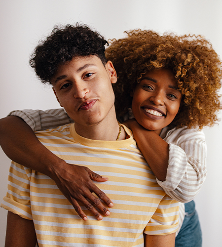 Two smiling individuals, one standing behind the other with arms around their shoulders in a friendly pose